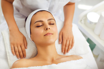 Fototapeta na wymiar Hands of cosmetologist relaxing on towel near womans face after facial massage