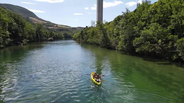Aerial view of people paddling in a kayak canoe up the green river and having fun. Group of active young friends paddling up the beautiful green river valley in a canoe in Millau, France.