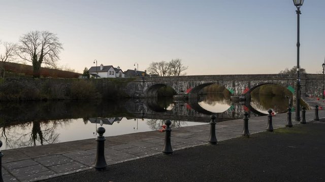 Holy Grail or Day to Night Time Lapse of town village with bridge and street lights along a river in Ireland.