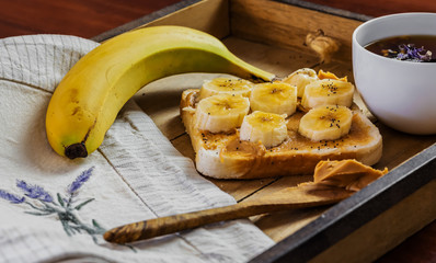 wooden tray with vegan breakfast with banana, tea, sandwich