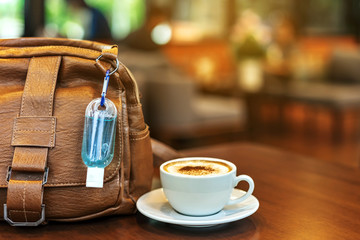 Mini alcohol gel bottle to kill Corona Virus(Covid-19) hang on a brown leather shoulder bag with hot coffee on table in cafe.New normal lifestyle.Health care concept.Selective focus on alcohol gel