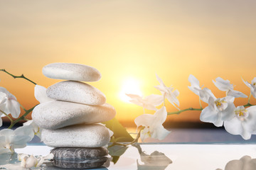 Orchid flowers and spa stones in water outdoors at sunset
