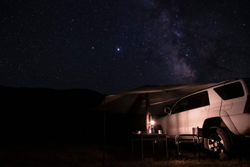 Car with tent or marquee with mountains silhouette and many stars background. Overlanding, car tourism concept. Adventure travel. Outdoor landscape. Night sky, stars background.