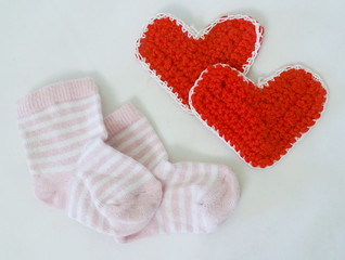 With the birth. Children's socks and red knitted hearts on a white background
