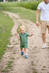 Fototapeta premium Cute little boy walking along the path on the background of reeds. His father is with him. Walk in park. Family life.