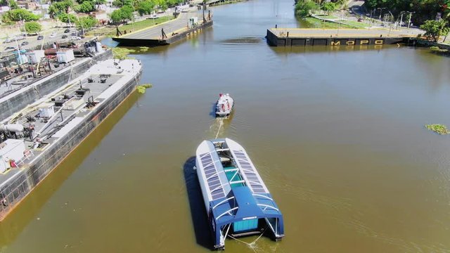 Overhead View Of Ocean Cleanup Ship Interceptor 004 On Ozama River Being Pulled By Tug Boat In Narrow Harbor Port In Downtown Santo Domingo, Dominican Republic, Above Aerial Static