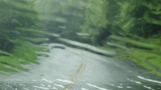 Abstract lines, circles and patterns of wet water rain drops pouring down, colliding, splashing and splattering on window windshield of car on rainy day, handheld pov passenger, slow motion