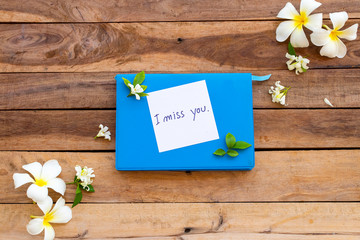 i miss you message card handwriting on blue diary book with white flowers frangipani ,jasmine arrangement  flat lay style on background wooden