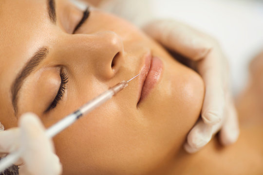 Hands of cosmetologist making botox injection in female upper lip with syringe