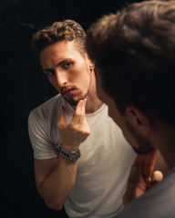 Vertical shot of a handsome caucasian male looking at himself in a mirror
