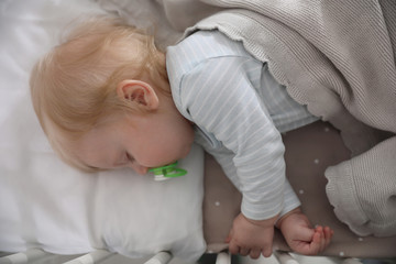 Cute little baby with pacifier sleeping in crib, top view. Bedtime