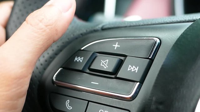 Close up of finger pressing the audio control buttons to increase or decrease the volume on the steering wheel when driving.