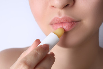 Naklejka premium Woman applying hygienic lipstick on lips against white background, closeup