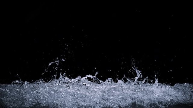 Abstract splashing water wave isolated on black background. Studio super slow motion shot with clear pure drinking water on cutout high key background splashing onto pov glass in high speed.