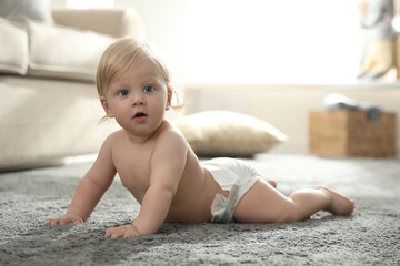 Cute little baby in diaper on carpet at home