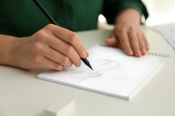Naklejka premium Woman drawing with pencil in notepad at white table, closeup