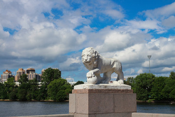 Fototapeta premium History and modernity - a white lion statue and a modern residential complex against the backdrop of a blue sky with clouds. St. Petersburg.