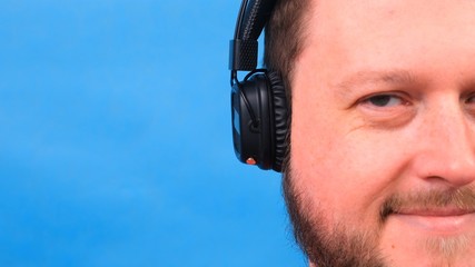 Bearded funny cute fat man in a pink T-shirt listens to music and dances on a blue background