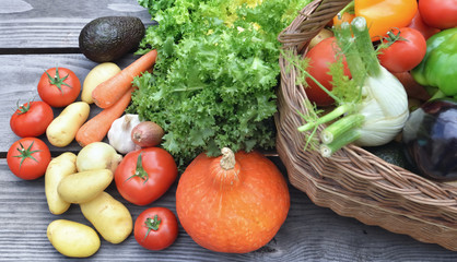 various  and colorful vegetables on a wooden table with a wicker basket