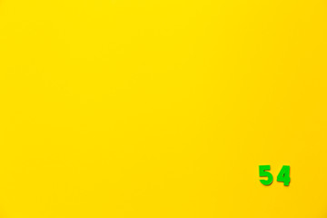 A green plastic toy number fifty-four is located in the lower right corner on a yellow background