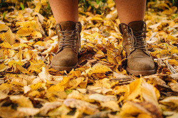 Close up photo of someone's feet in classic leather boots standing on the ground with yellow autumn leaves