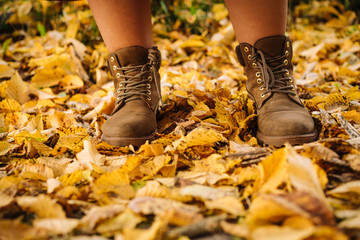 Close up photo of someone's feet in classic leather boots standing on the ground with yellow autumn leaves