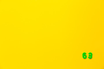 A green plastic toy number sixty-three is located in the lower right corner on a yellow background