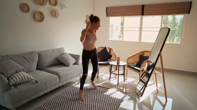 happy woman dancing and singing on the remote control in front of the mirror. having fun enjoying playful dance