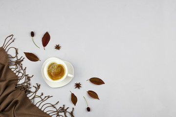 Autumn composition. Cup of coffee with cinnamon, autumn leaves and plaid on grey background. Flat...