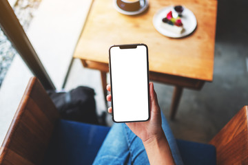 Top view mockup image of a woman holding mobile phone with blank white desktop screen in cafe