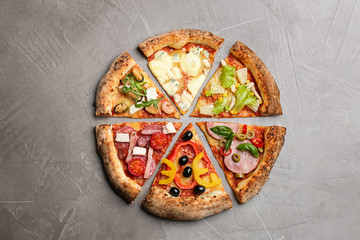 Slices of different delicious pizzas on grey table, flat lay