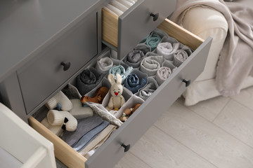 Modern open chest of drawers with clothes and accessories in baby room