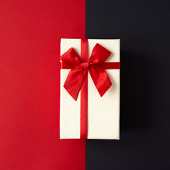 White present with red ribbon on the bright red and black background . Festive backdrop for holidays: Birthday, Valentines day, Christmas, New Year, Black Friday