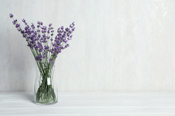 Beautiful lavender flowers in glass vase on white wooden table against light background. Space for...