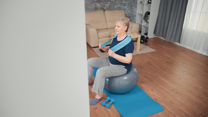 Fototapeta na wymiar Cheerful senior woman exercising on balance ball. Old person training at home sport healthy lifestyle, elderly fitness exercise workout in apartment, activity and healthcare