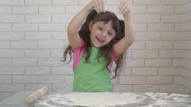 A child roll out dough. Happy little girl having fun with flour in the kitchen.