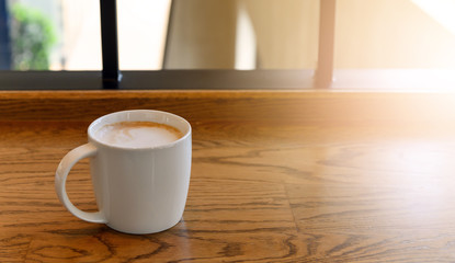white coffee cup with hot cappuccino coffee on wooden table in coffee cafe. copy space for adding text