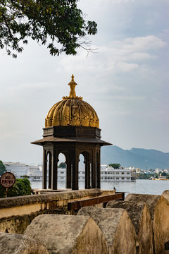 A Lake side tower with golden dome with buildings, lake, mountain, tree and beautiful sky in background. No entry sign near it.