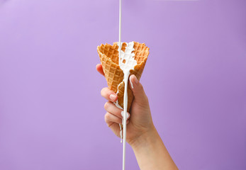 Pouring molten ice cream into wafer cone held by woman on violet background, closeup