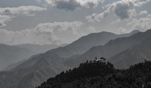 A Temple on top of hill between beautiful mountains and cloudy sky above.
