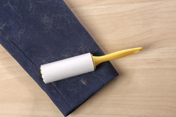 Lint roller and sleeve of jacket covered with hair on wooden table, flat lay