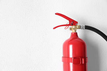 Naklejka premium Fire extinguisher hanging on white wall, closeup. Space for text
