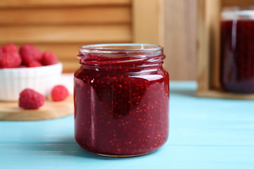 Delicious raspberry jam on light blue wooden table, closeup