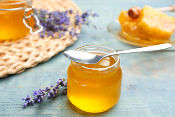 Tasty honey in glass jar and lavender flowers on light blue wooden table