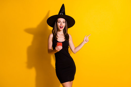 Photo excited spooky witch lady use smartphone point index finger copyspace mysterious boo enchant adverts wear black cap headwear skirt isolated bright shine color background
