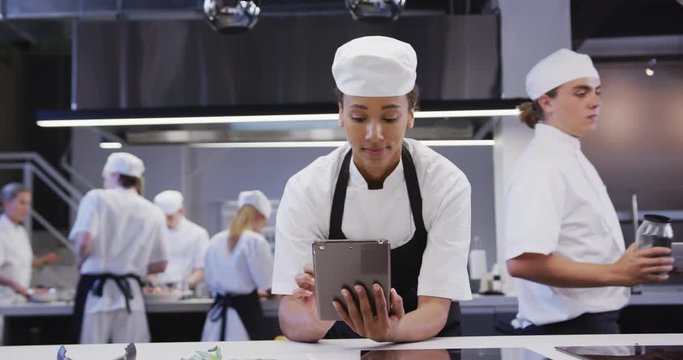 African American Female Chef Wearing Chefs Whites In A Restaurant Kitchen, Using A Tablet