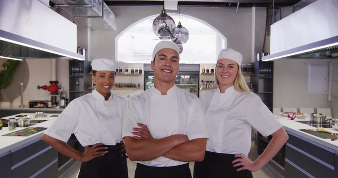 Multi-ethnic chefs wearing chefs whites in a restaurant kitchen looking at camera and smiling 