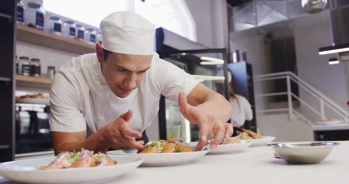 Mixed race male chef wearing chefs whites in a restaurant kitchen, putting food on a plate