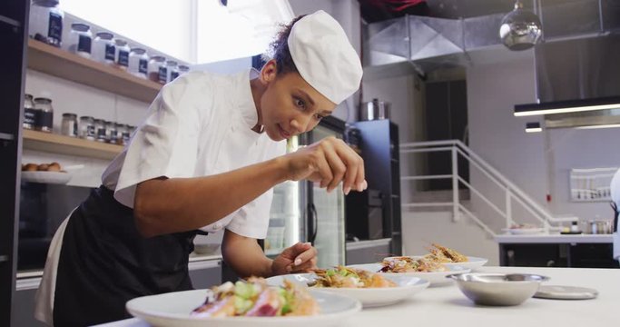 African American female chef wearing chefs whites in a restaurant kitchen, putting food on a plate