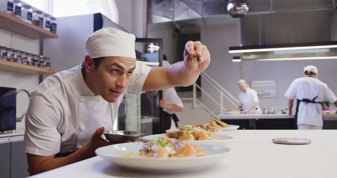 Professional mixed race male chef in a restaurant kitchen, putting food on a plate